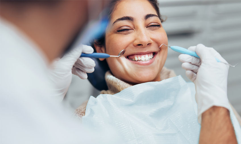 Happy woman getting dental checkup at dentistry. Dentist using dental equipment for examination of teeth of a female patient