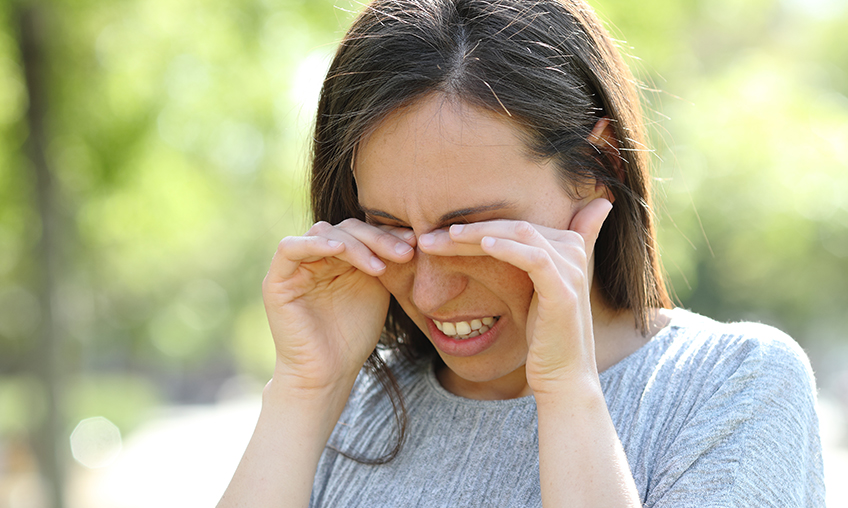 Disgusted woman rubbing her eyes standing outdoors in a park