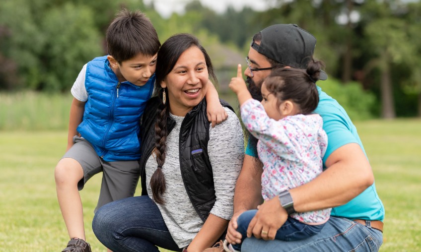 native american family of four sitting on grass talking playfully