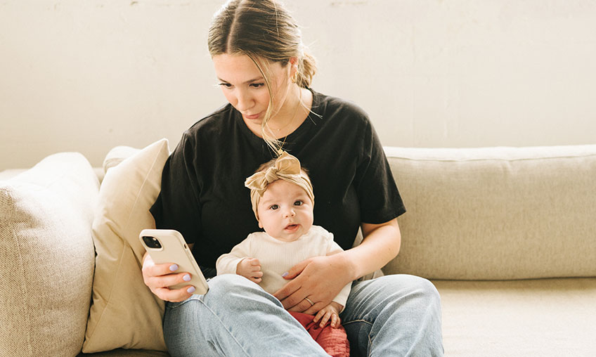 madre texteando desde el celular con el bebé en el regazo