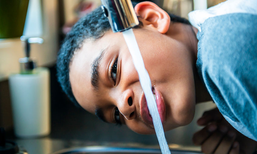 niño tomando agua del caño de la cocina