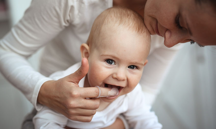 madre lavándole los dientes a su bebé con un cepillo de dientes de dedo