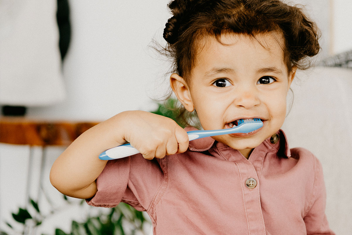 Una niña vestida de rosa lavándose los dientes
